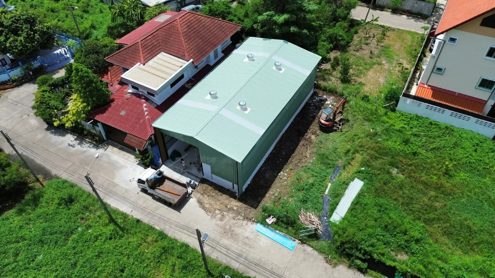 ภาพมุมสูงช่วงงานใกล้แล้วเสร็จ มีรถบรรทุกและรถขุดเก็บงานรอบอาคาร